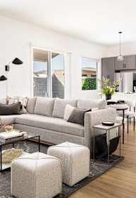 A modern living room with a grey sofa, a glass coffee table, and a black rug.