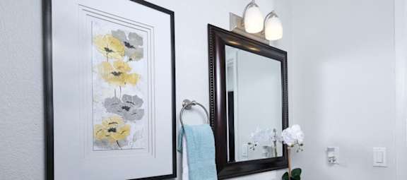 Bathroom in Fifteen 50 Apartments Las Vegas with floral art, vanity mirror, and sink with storage.