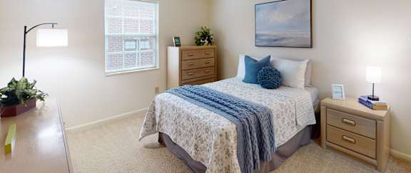A bedroom with a bed, nightstand, and a plant on a wooden table.