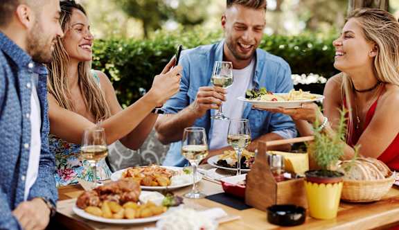 Four people are sitting at a table with plates of food and glasses of wine.