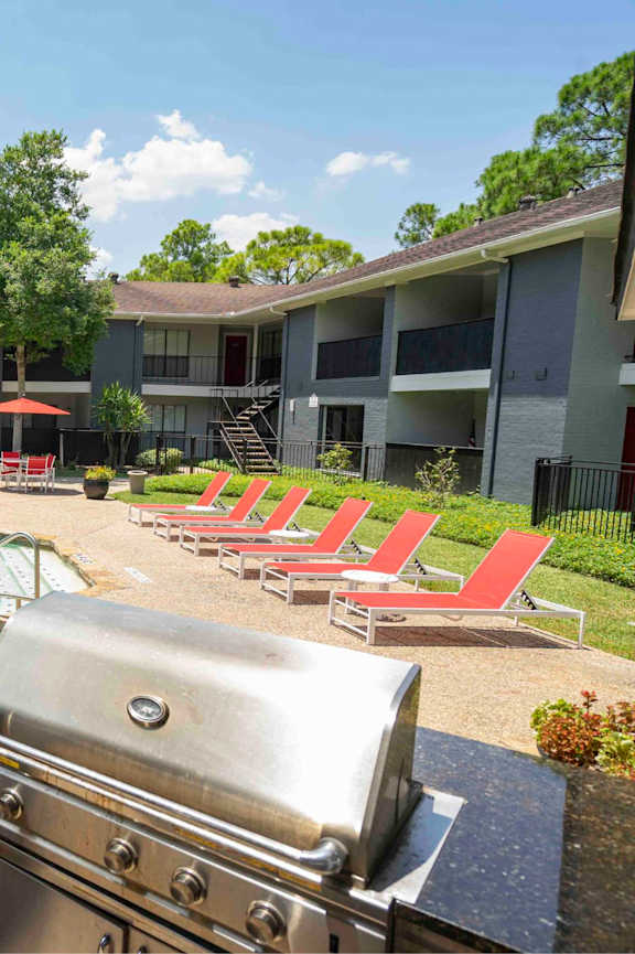 A grill is in the foreground of a photo showing a pool and apartment complex.