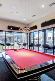 A game room with a red pool table and tv and glass windows and mini fridge