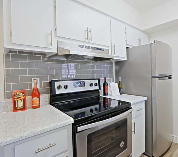View of Kitchen with white cabintery, a stove, a refrigerator, and subway tile backsplash at Spring Meadow Apartments in Glendale, AZ