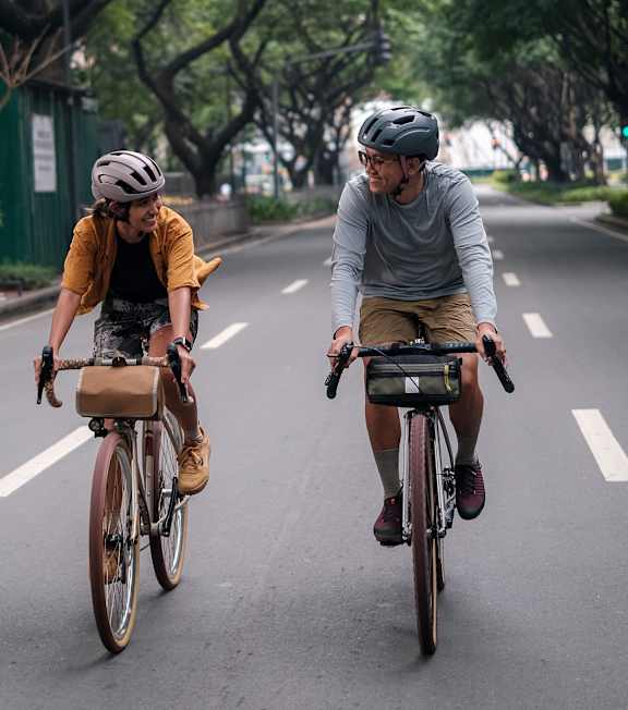 Two people riding bicycles on a tree-lined street.