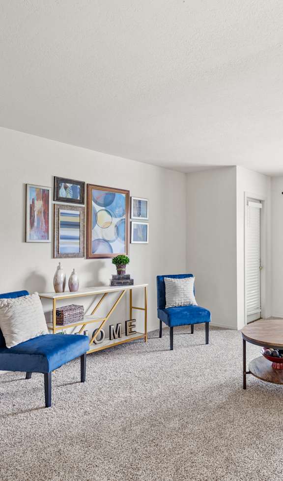 A living room with a white couch, blue chairs, and a painting on the wall.