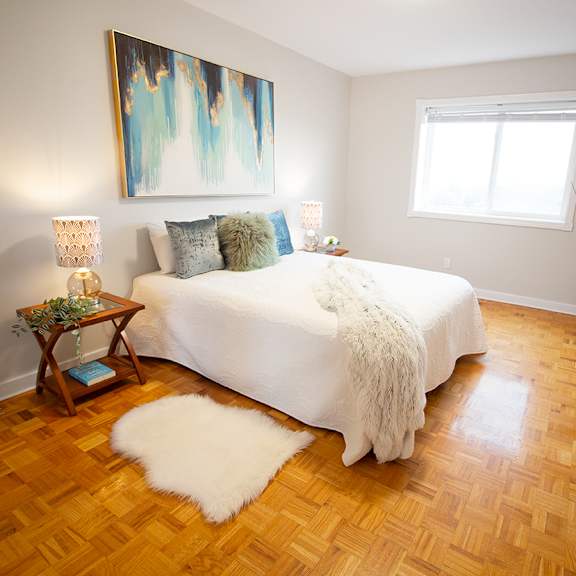 A bedroom with a large bed, a painting on the wall, and a wooden floor.
