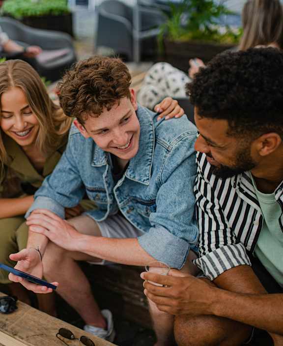 Four people sitting around a table looking at a cell phone.
