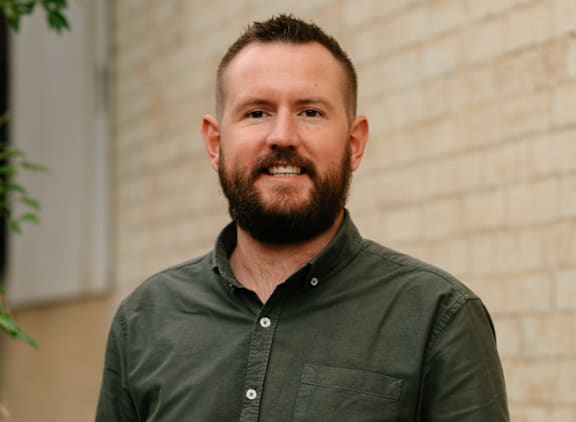 A man with a beard is standing in front of a brick wall.