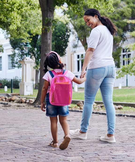 A woman and a child are walking together on a paved path in a park.