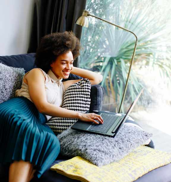 A woman with an afro is sitting on a couch with a laptop.
