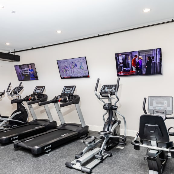 a gym with cardio machines and televisions on the wall