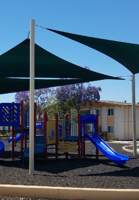 a playground with a blue slide and a purple slide in front of an apartment complex