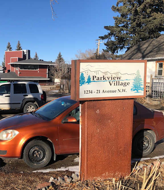 A sign for Parkview Village stands in front of a car.