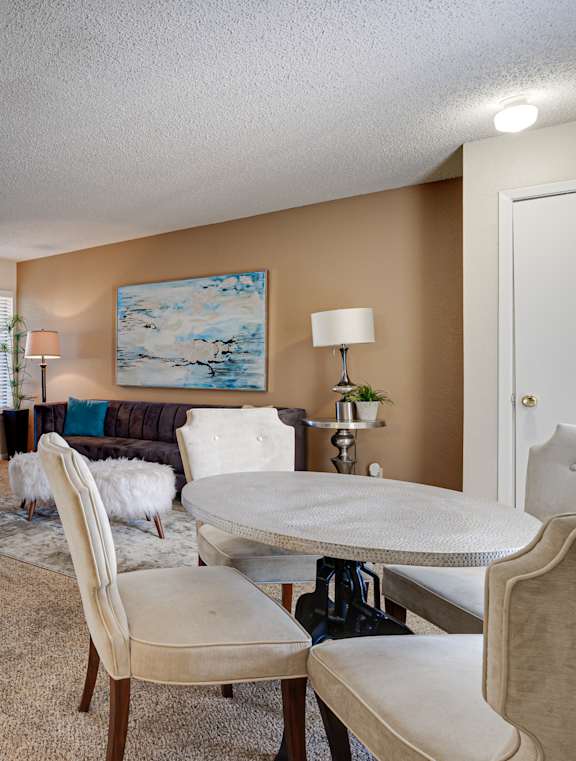 A kitchen with a refrigerator, a dining table with chairs, and a painting on the wall.