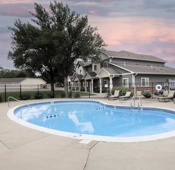 A large outdoor swimming pool surrounded by a fence and a house in the background.