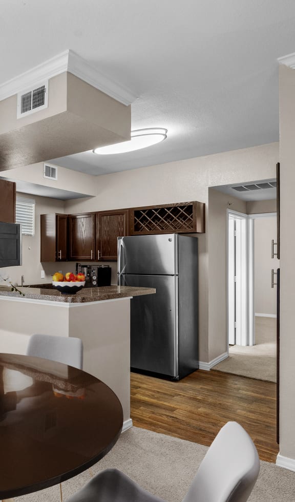 a dining room with a table and chairs and a kitchen with a refrigerator at The Clairborne Apartment Homes, Grand Prairie, TX, 75050