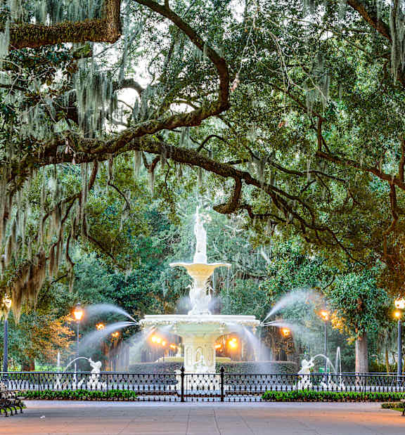 A park with a fountain and benches under a canopy of trees.