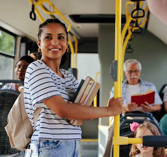 A woman in a striped shirt is holding onto a pole in a bus.