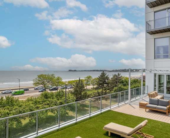 A balcony with a chair and a table overlooking a beach.