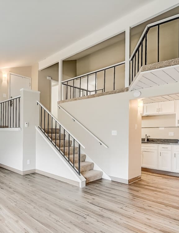an empty living room with a staircase and a kitchen