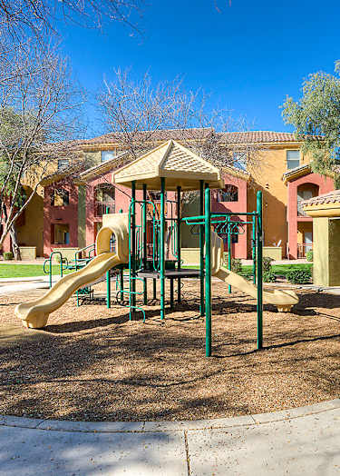 A basketball court with a bench on the side and two houses in the background.