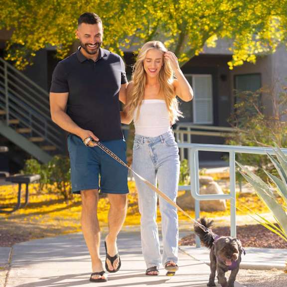 A man and woman walking a dog on a leash.