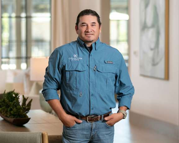 A man in a blue shirt and jeans stands in a room.