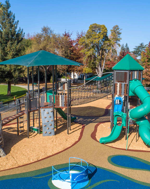 A playground with a blue slide and a green umbrella.