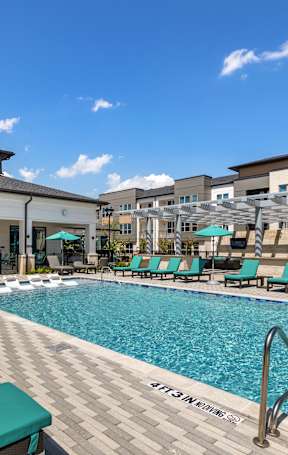 A pool area with sun loungers and a building in the background.