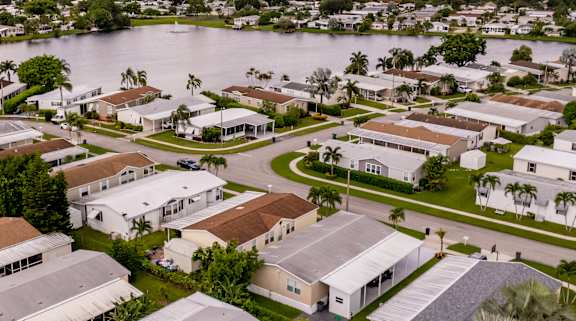 A large white building with a grey roof is surrounded by other buildings and trees.