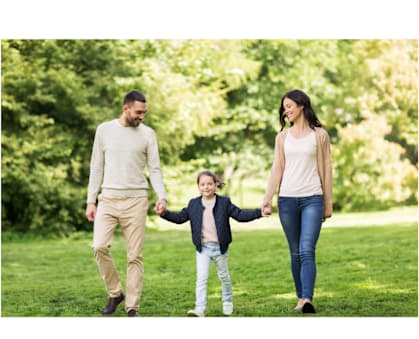 A family of three is walking hand in hand in a park.