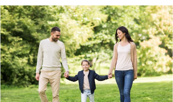 A family of three is walking hand in hand in a park.