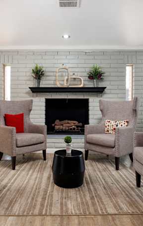 Four chairs with red pillows are arranged around a fireplace.