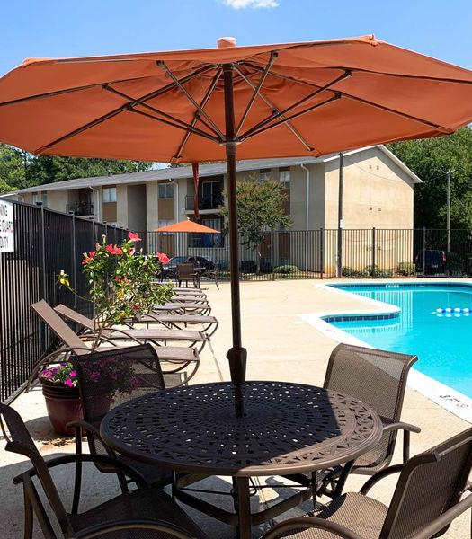A table with chairs and an umbrella is in front of a pool.