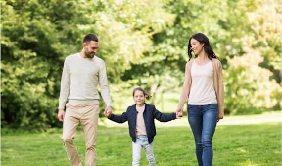 A family of three is walking hand in hand in a park.