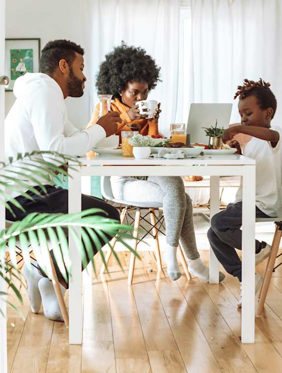 group of people sitting around a table eating at a laptop