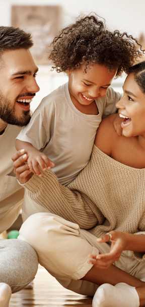 A man and a woman are sitting on the floor with a child between them, all are smiling and appear to be happy.