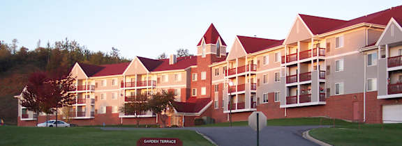 A large building with a red roof is surrounded by a grassy area and a road.