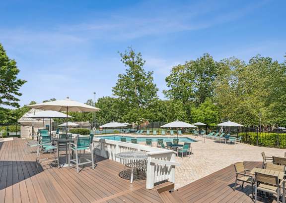 A wooden deck with chairs and umbrellas overlooking a pool.