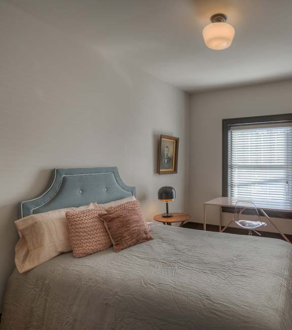 A bedroom with a bed, nightstand, and a plant.
