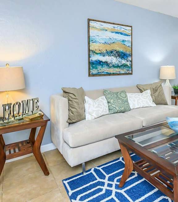 A living room with a white couch, a blue coffee table, and a painting on the wall.
