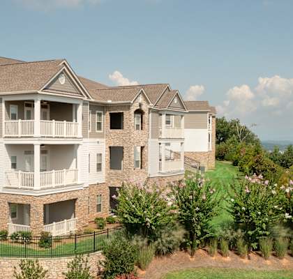 A large, multi-story residential building with a well-manicured lawn and a stone wall in front.