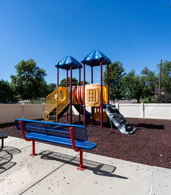 A playground with a blue bench, a yellow slide, and a red and blue swing set.