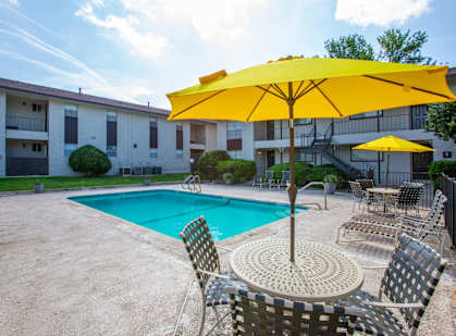 A yellow umbrella shades a table and chairs by a pool.