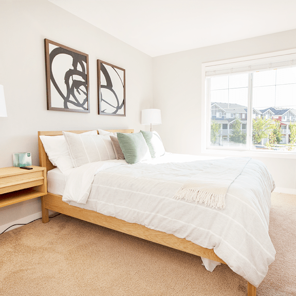 A bedroom with a large bed, a painting on the wall, and a wooden floor.