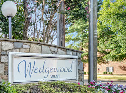A sign that says "Wedgewood West" is surrounded by greenery and flowers.