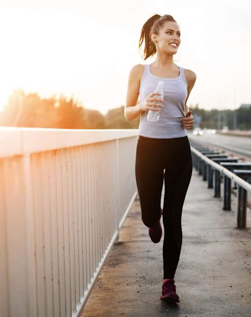 A woman is running on a bridge holding a water bottle.