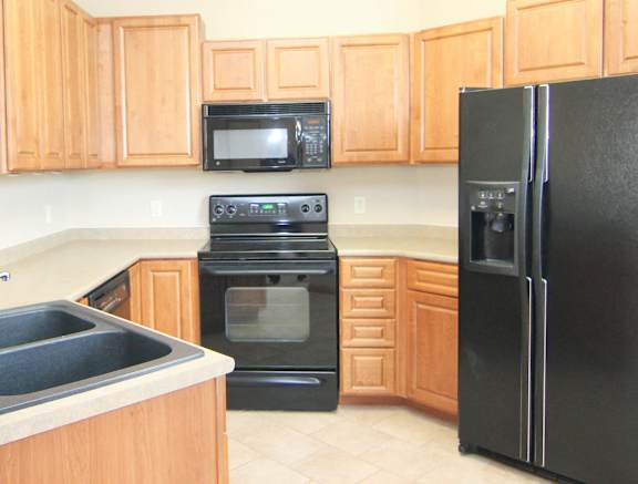 Kitchen with warm brown cabinets, black appliances, and granite breakfast bar.
