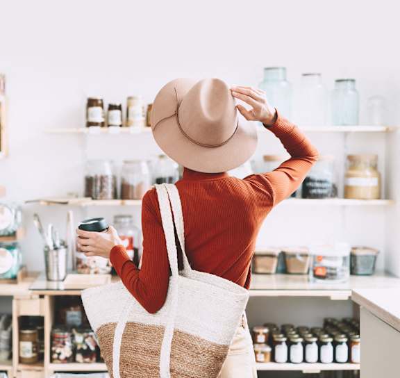 A woman in a hat is shopping in a store with a variety of items on the shelves.