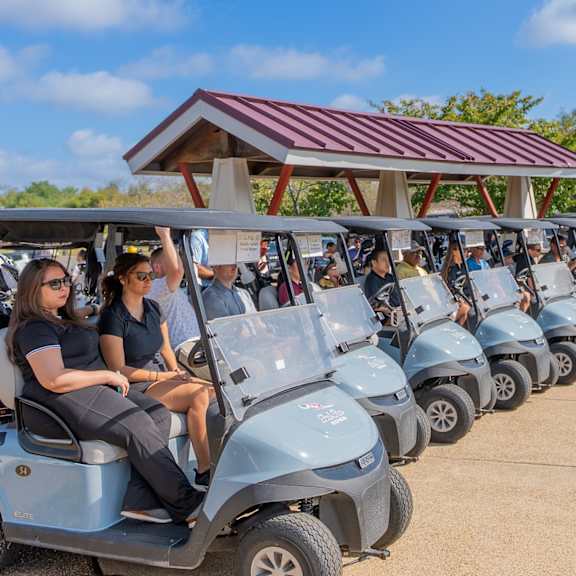 A group of people are riding in a line of blue golf carts. at Lakes Edge Apartments, North Carolina